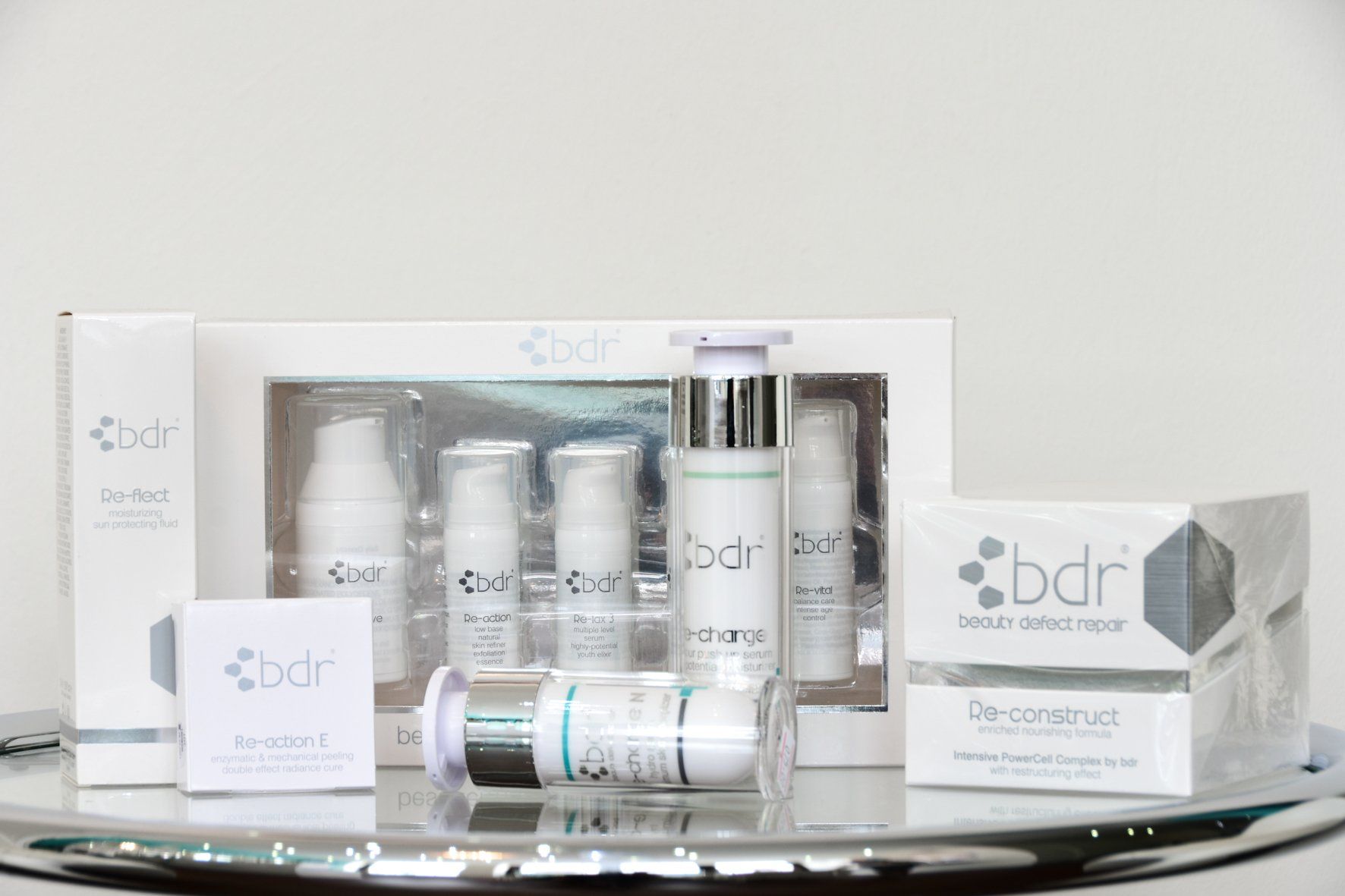 Kollektion weißer Hautpflegeprodukte mit dem „bdr“-Logo auf einer reflektierenden Oberfläche. Mehrere Flaschen und eine Schachtel sind sichtbar.