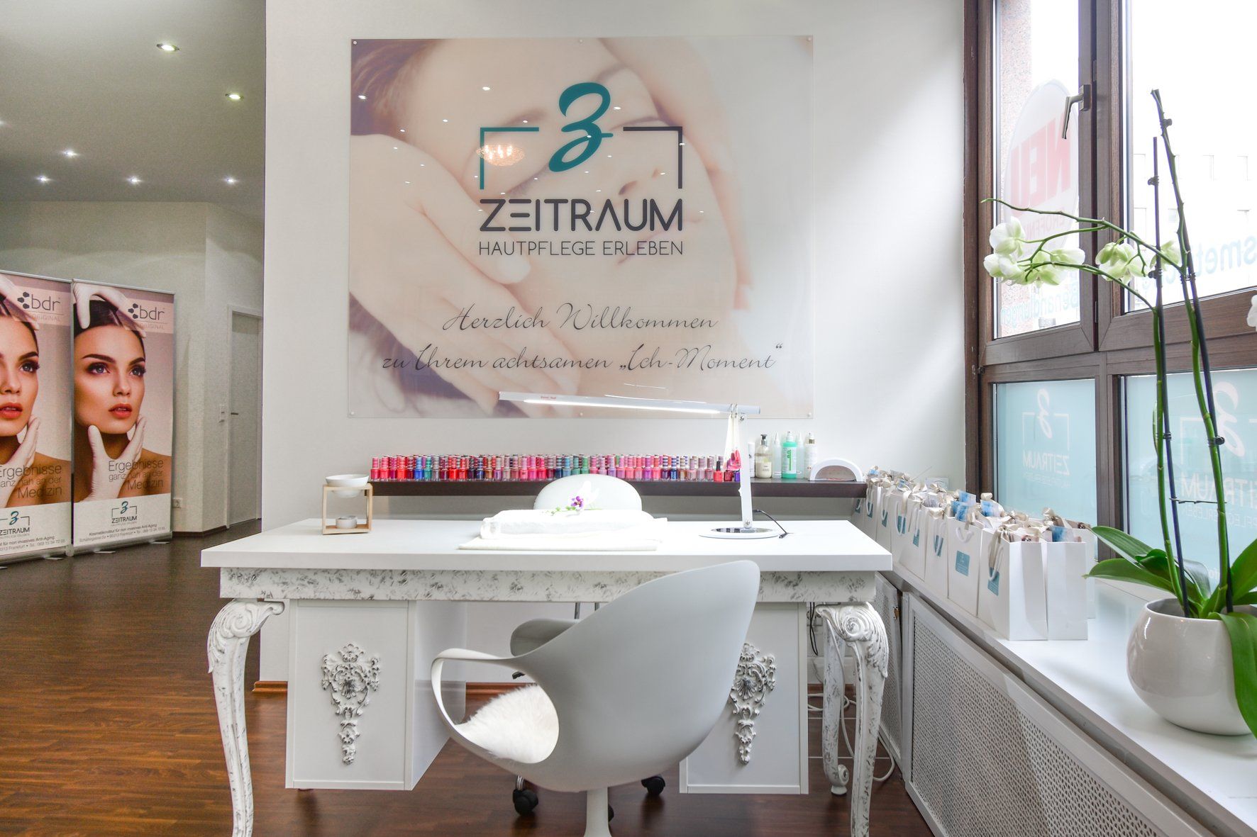 Ein weißer Maniküretisch in einem Schönheitssalon mit Nagellack, einem Stuhl und einem Fenster mit einer Orchidee im Topf.