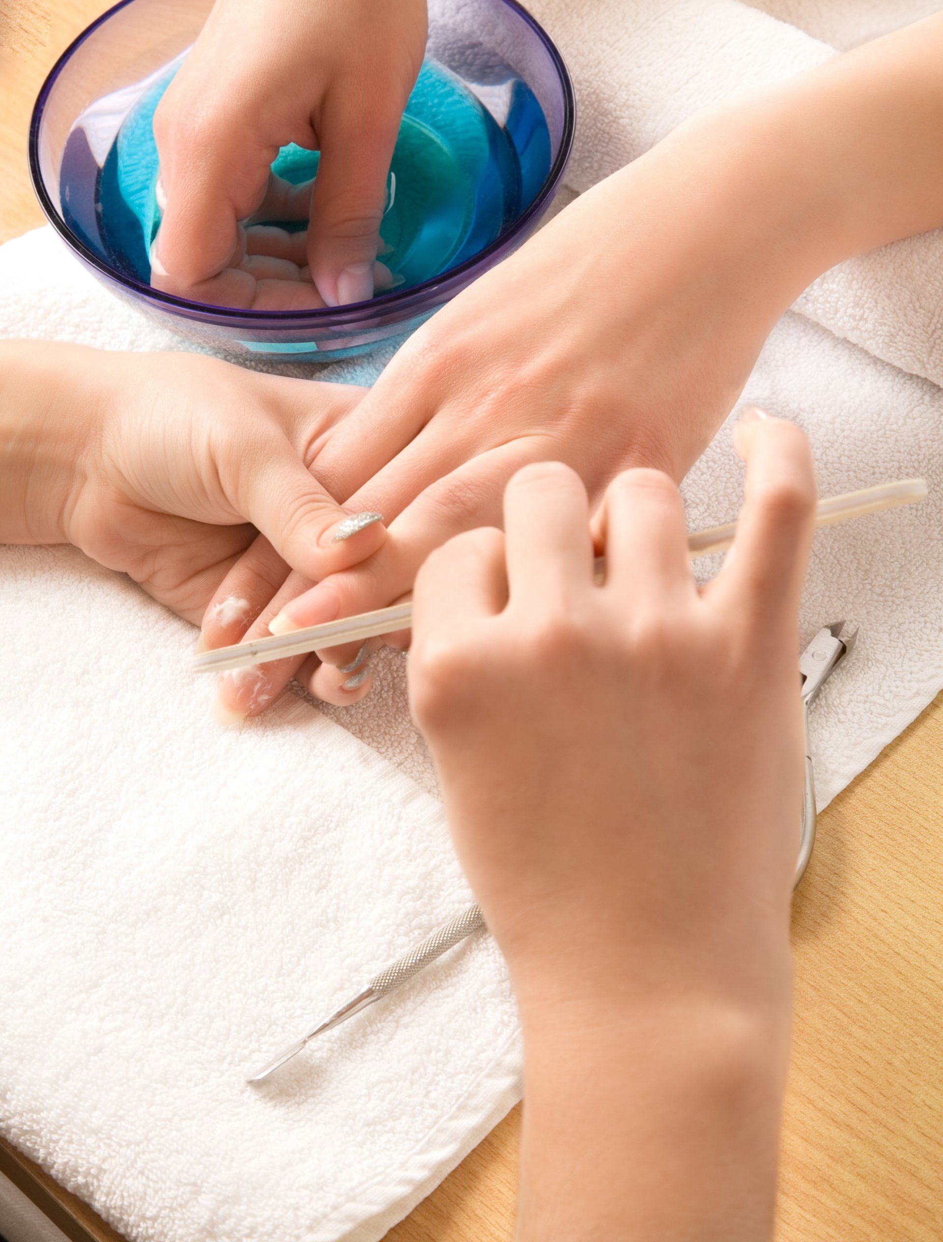 Eine Person bekommt eine Maniküre. Eine andere Person feilt die Nägel über einem weißen Handtuch, daneben steht eine Schale mit blauen Spa-Utensilien.