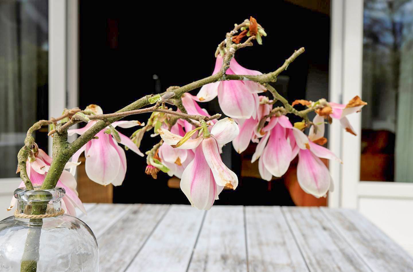 Op een houten tafel staat een vaas gevuld met roze bloemen.