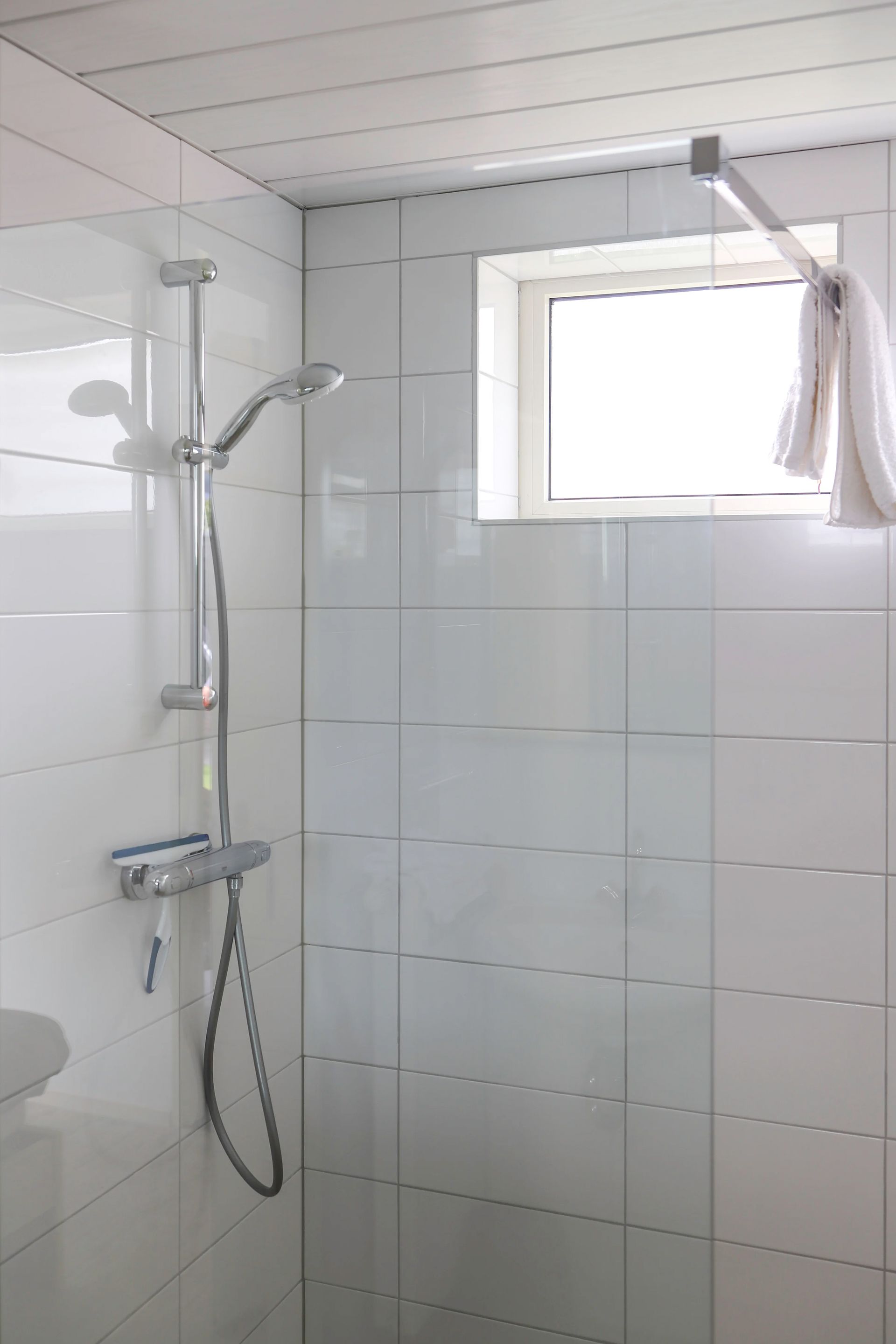 Een douche met een raam en een douchekop in een badkamer.