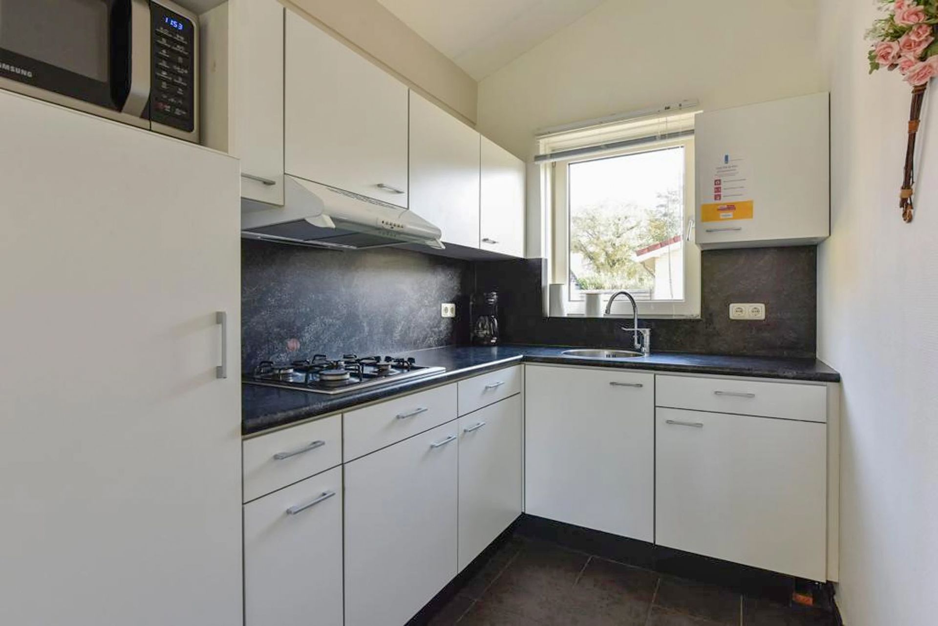 Een keuken met witte kasten, zwarte aanrechtbladen en een magnetron.