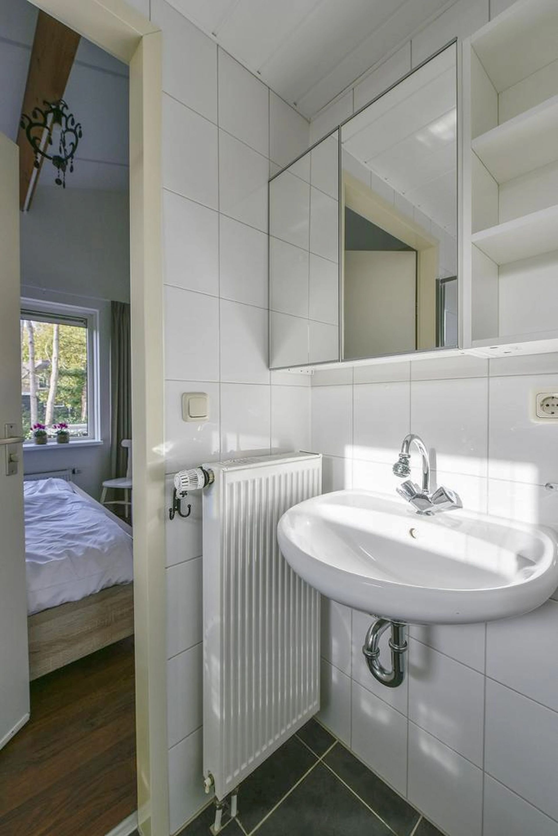 Een badkamer met wastafel, spiegel en radiator.