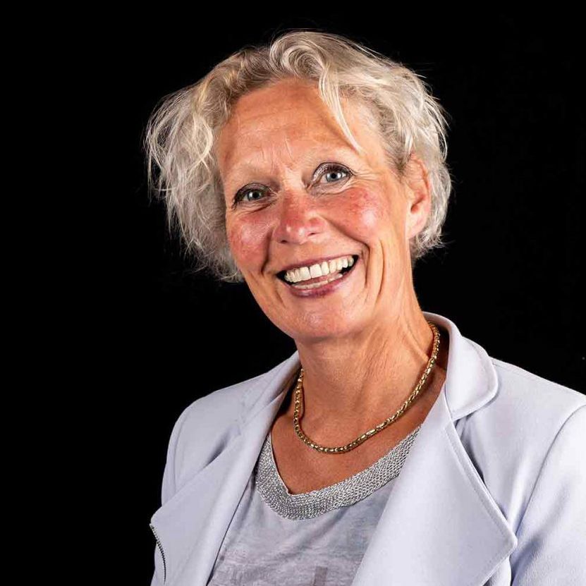 Een vrouw met een ketting en een jas lacht naar de camera.