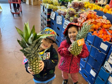 A boy and a girl are holding pineapples in a grocery store