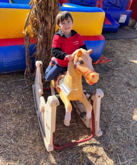 A young boy is riding a rocking horse in a pumpkin patch.