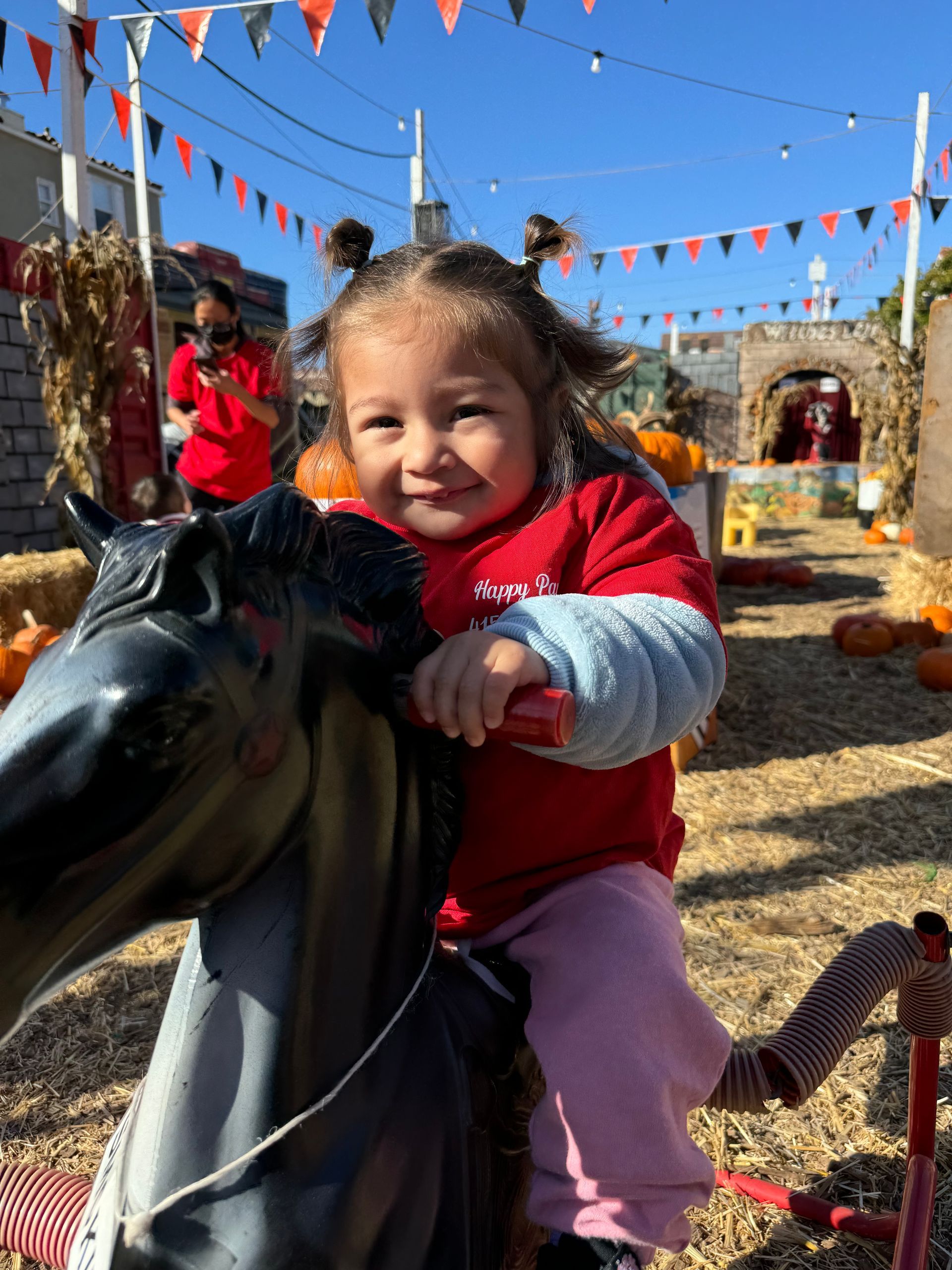 A little girl is riding a rocking horse at a pumpkin patch.