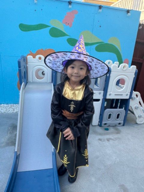 A little girl in a witch costume is standing next to a slide