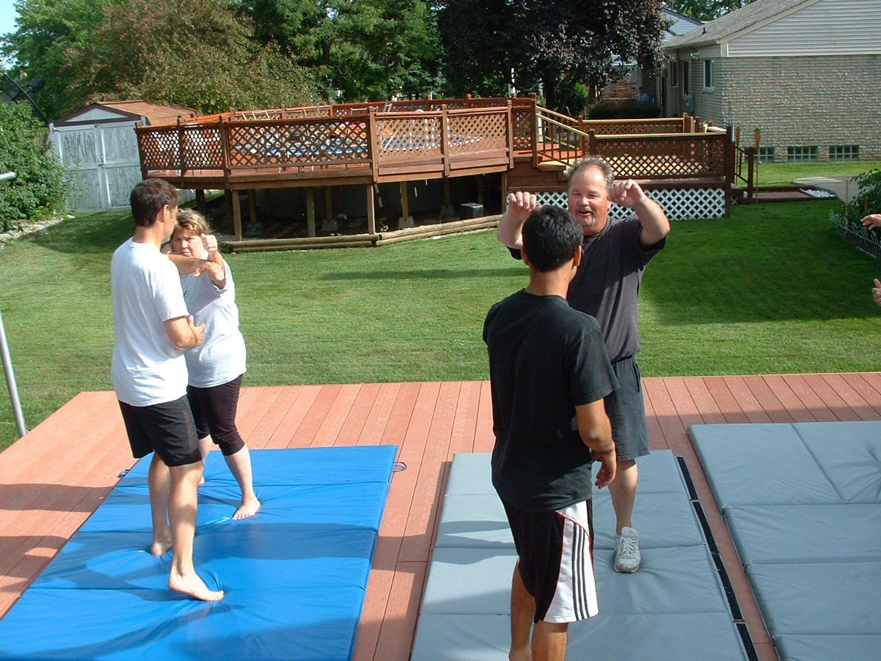 People practicing martial arts on mats in a backyard with a deck.