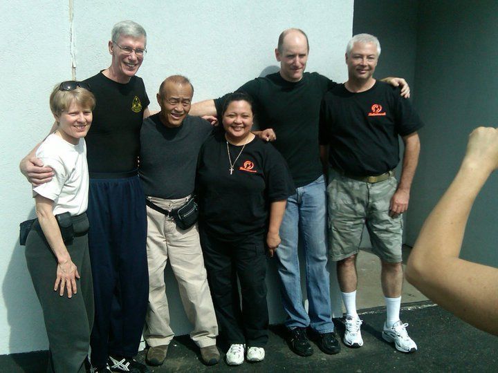 Group of people standing together outside, posing for a photo. They are smiling. A bicep is flexing on the right.