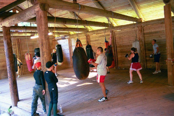 Boxing gym: People training with punching bags in a wooden structure.
