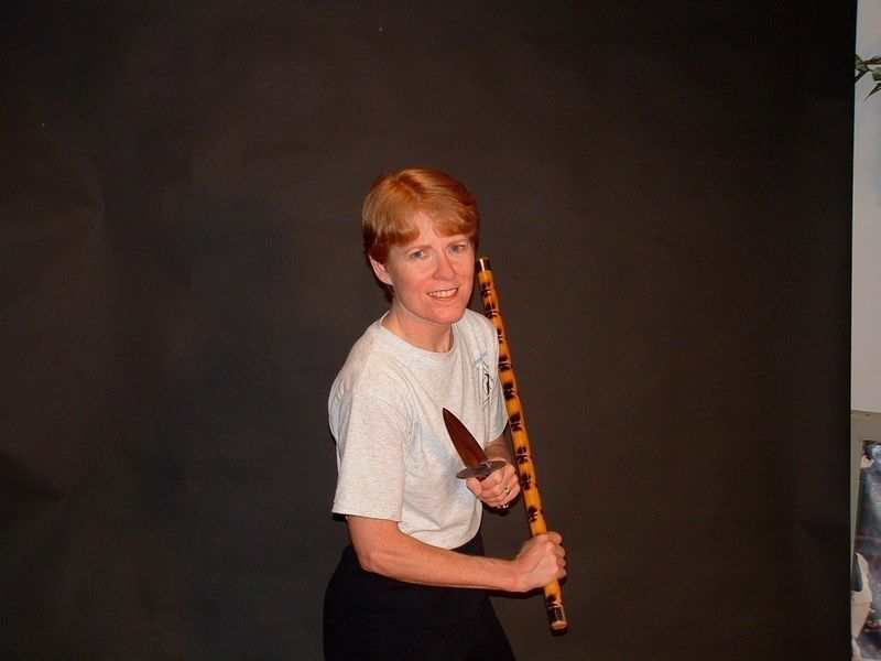 Woman holding a knife and a patterned stick, smiling, against a black backdrop.
