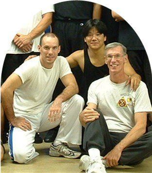 Three men posing, arms around each other. Men in athletic wear, smiles, inside.