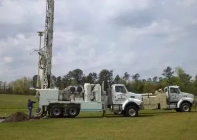 A man is standing next to a truck with a drilling rig attached to it.