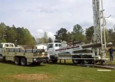 A truck with a drilling rig attached to it is parked in a grassy field.