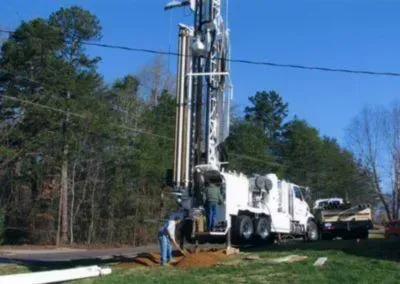 A truck is driving down a road next to a drilling rig.