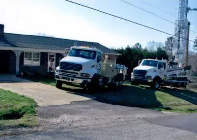 Two white trucks are parked in front of a house.