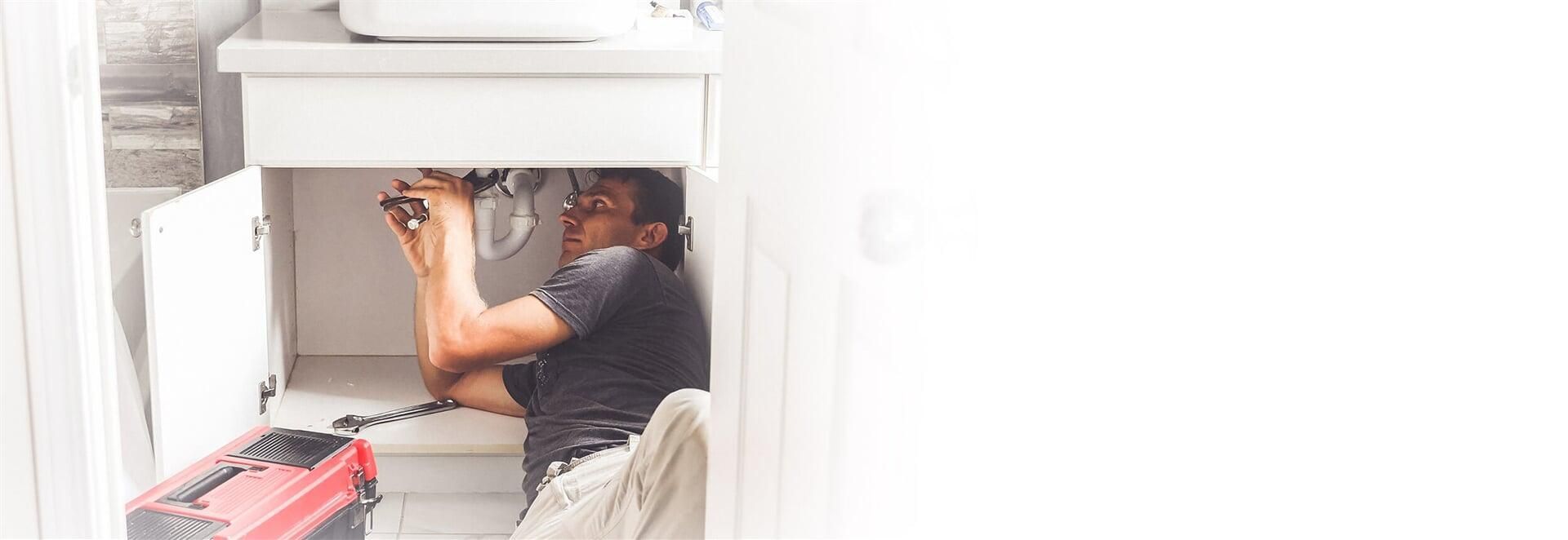 Un plomero está trabajando debajo de un lavabo en un baño.