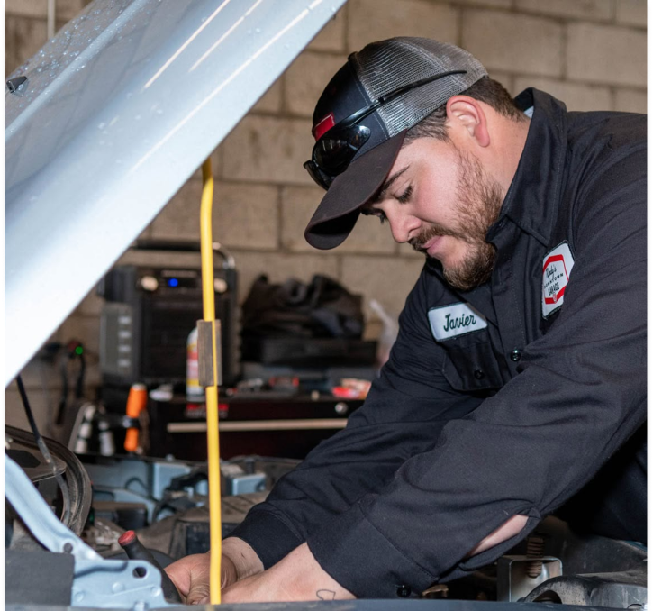 A person is working under the hood of a car with the hood open
