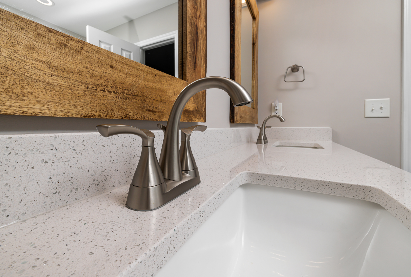 A modern bathroom vanity with a white speckled countertop, a white sink, and a brushed nickel faucet beneath a wood mirror.