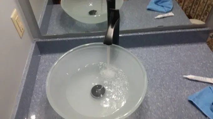 A black faucet running water into a frosted glass bowl sink on a speckled blue countertop.
