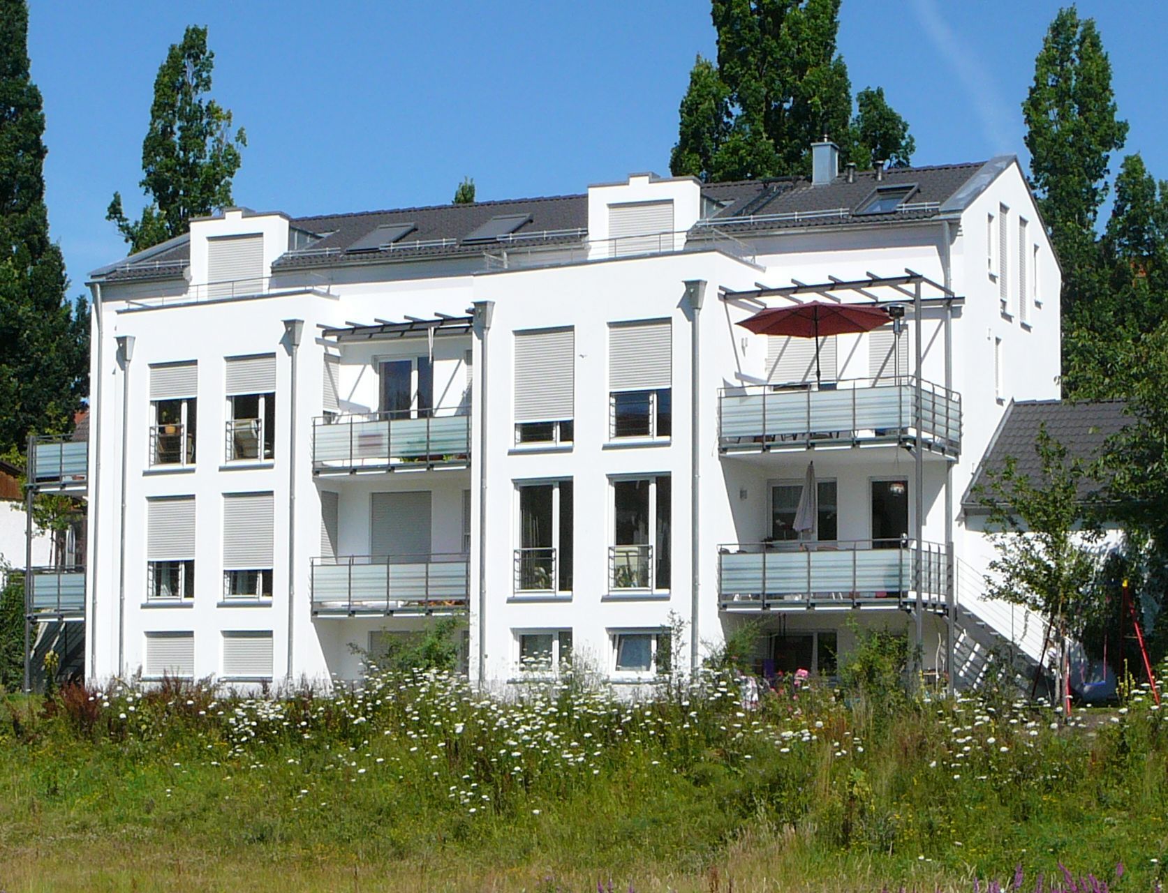 A white apartment building with a red umbrella on the balcony