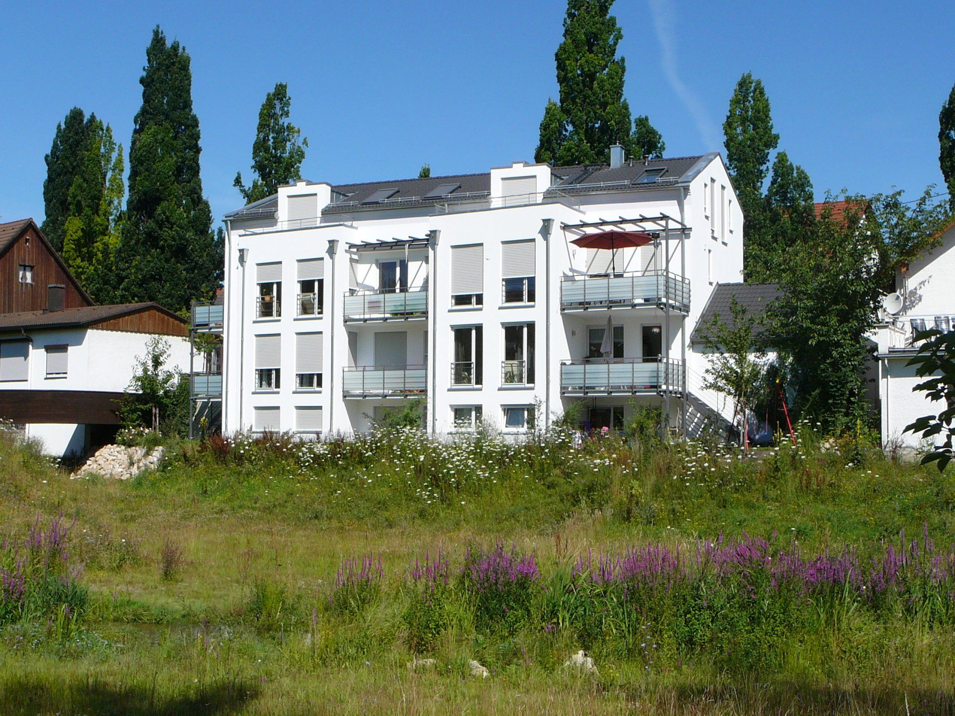 A large white building with balconies sits in the middle of a grassy field