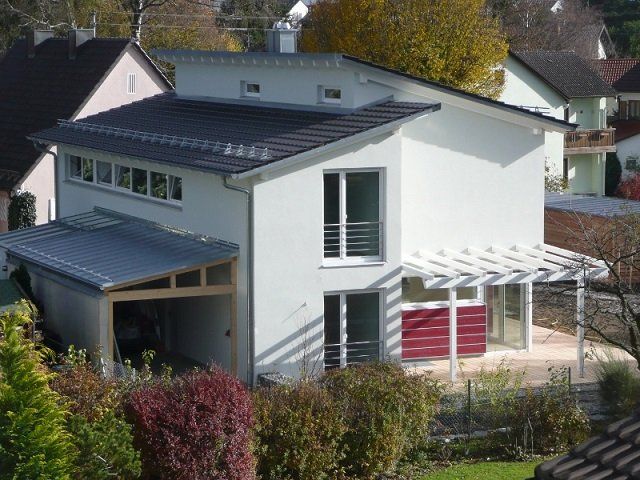 A white house with a black roof is surrounded by trees