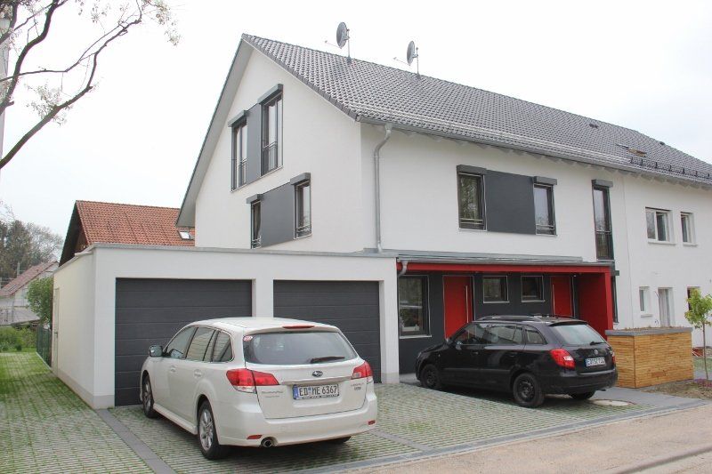 Two cars are parked in front of a white house.