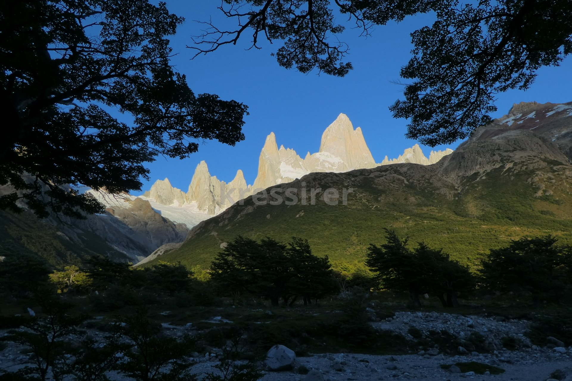 A mountain range with trees in the foreground and a blue sky in the background
