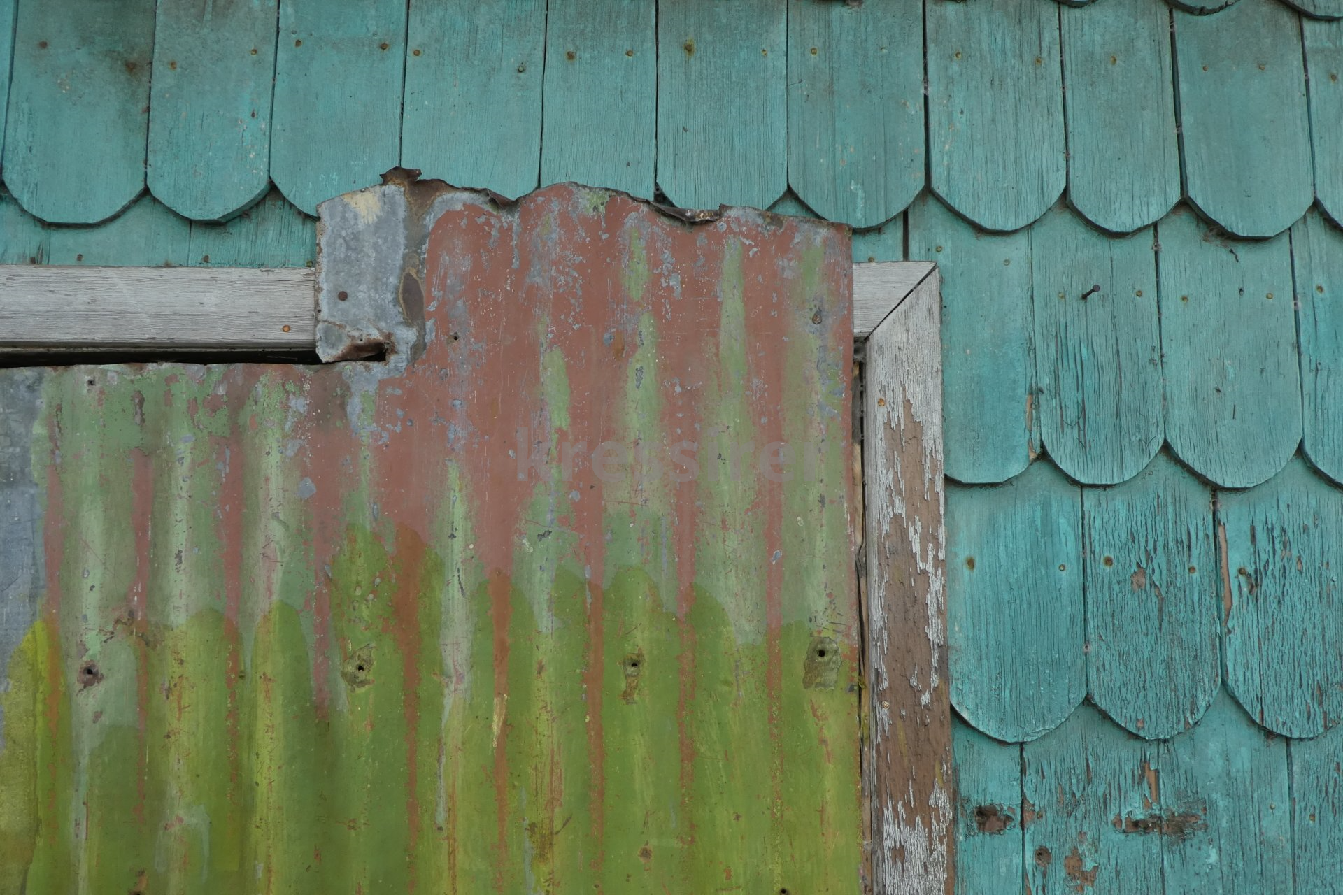 A close up of a wooden wall with a window and a rusty tin roof.