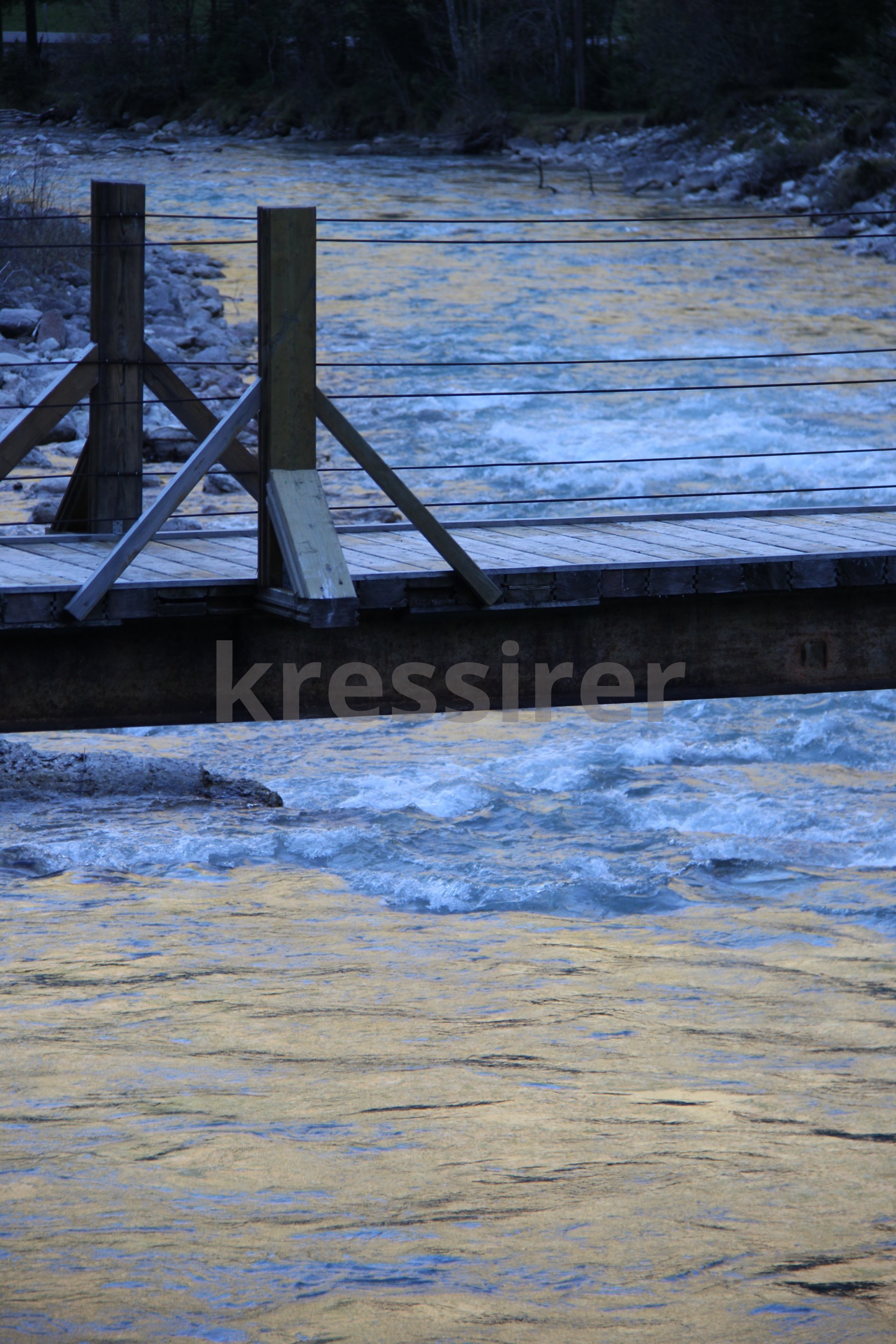 A wooden bridge over a river with ice on the water.