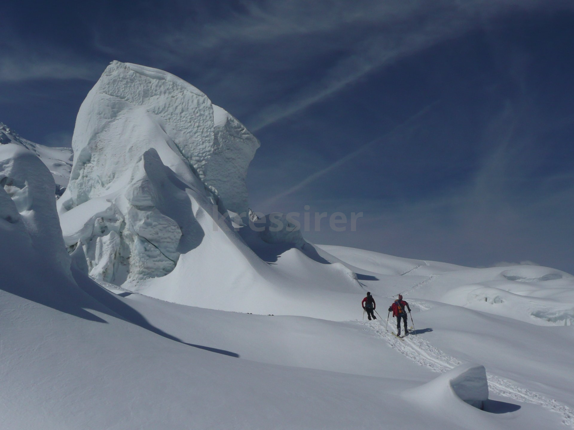 Two people skiing down a snow covered slope with a large rock in the background