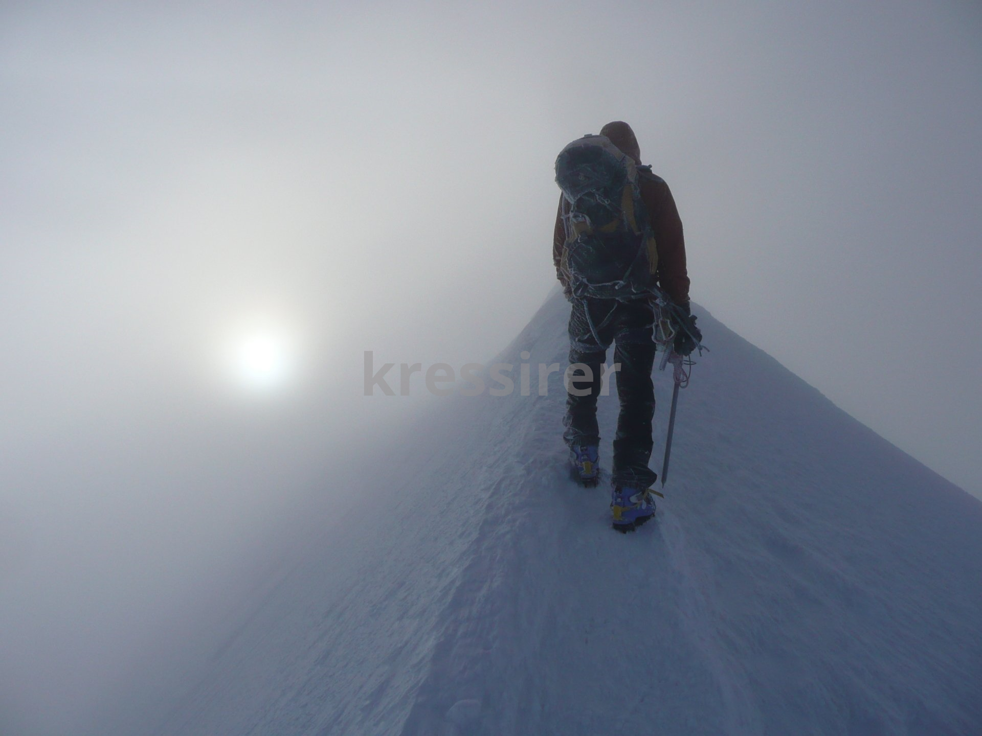 A person standing on top of a snow covered mountain with the sun shining behind them