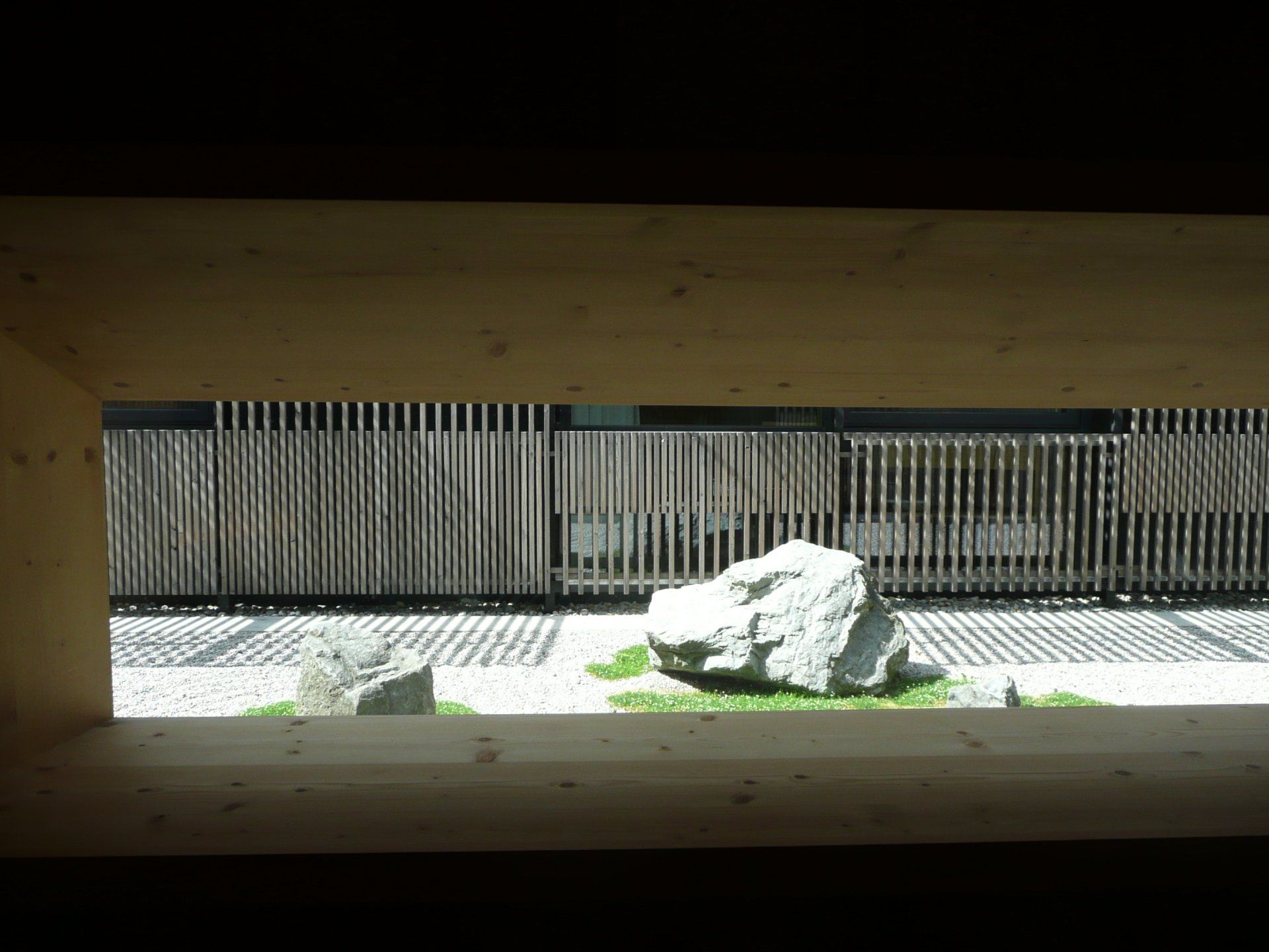 A view of a rock garden through a window with a fence in the background.