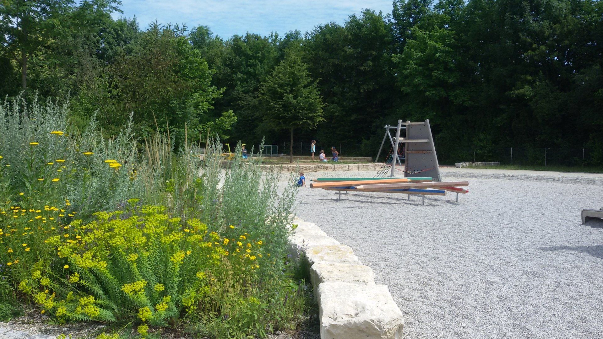 A playground with a slide and flowers in the foreground and trees in the background.