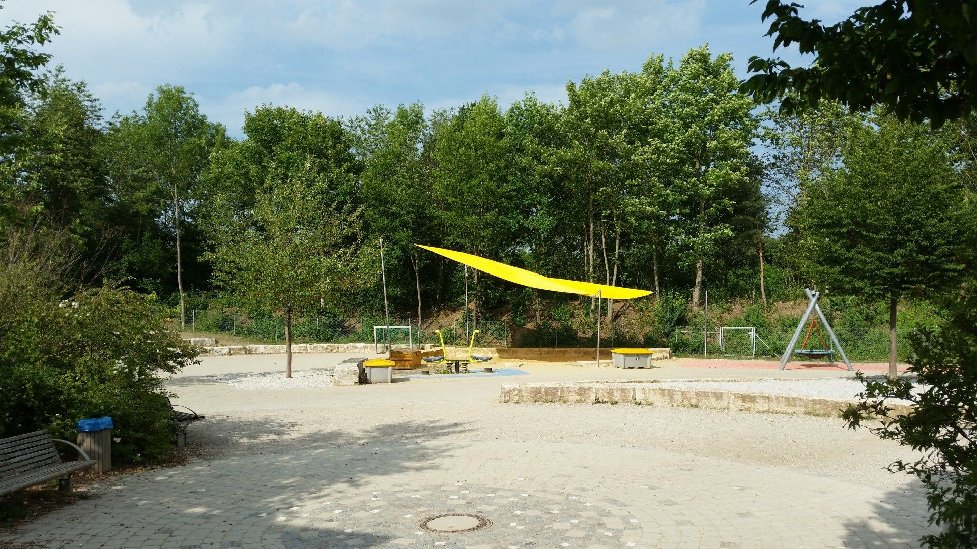 A playground with a yellow umbrella in the middle of it