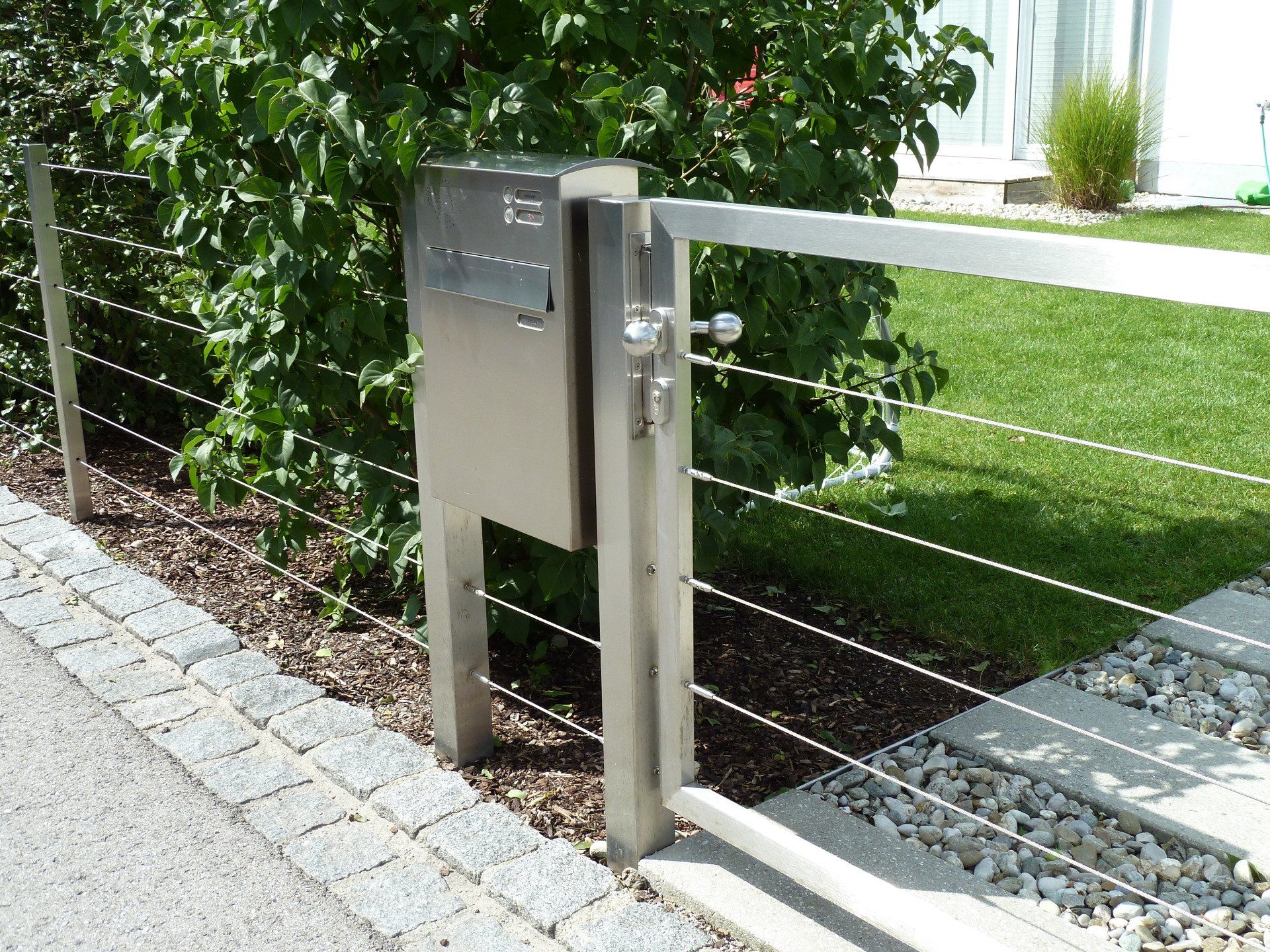 A stainless steel mailbox is attached to a wire fence