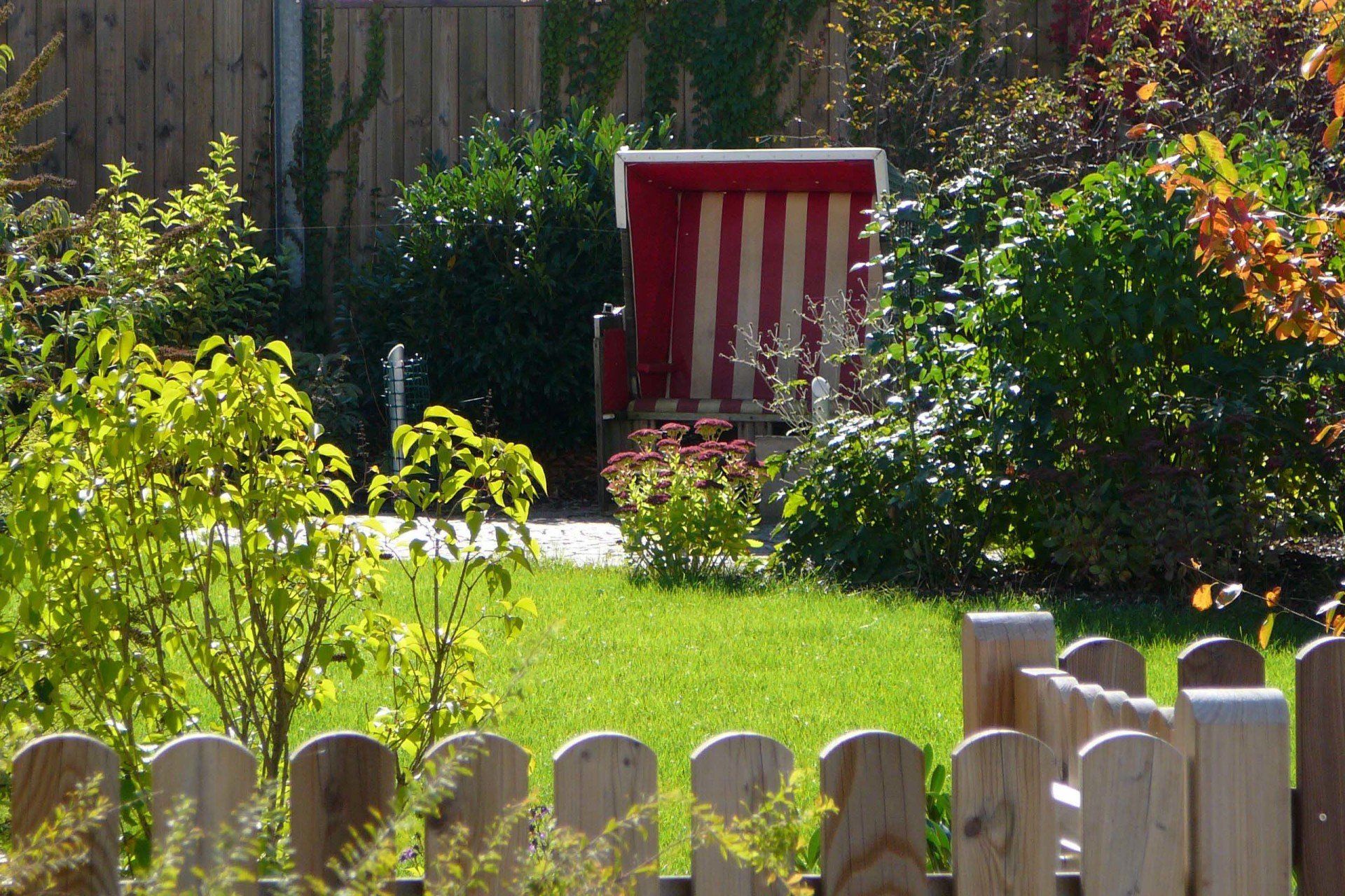 A wooden fence surrounds a garden with a red and white chair in the background
