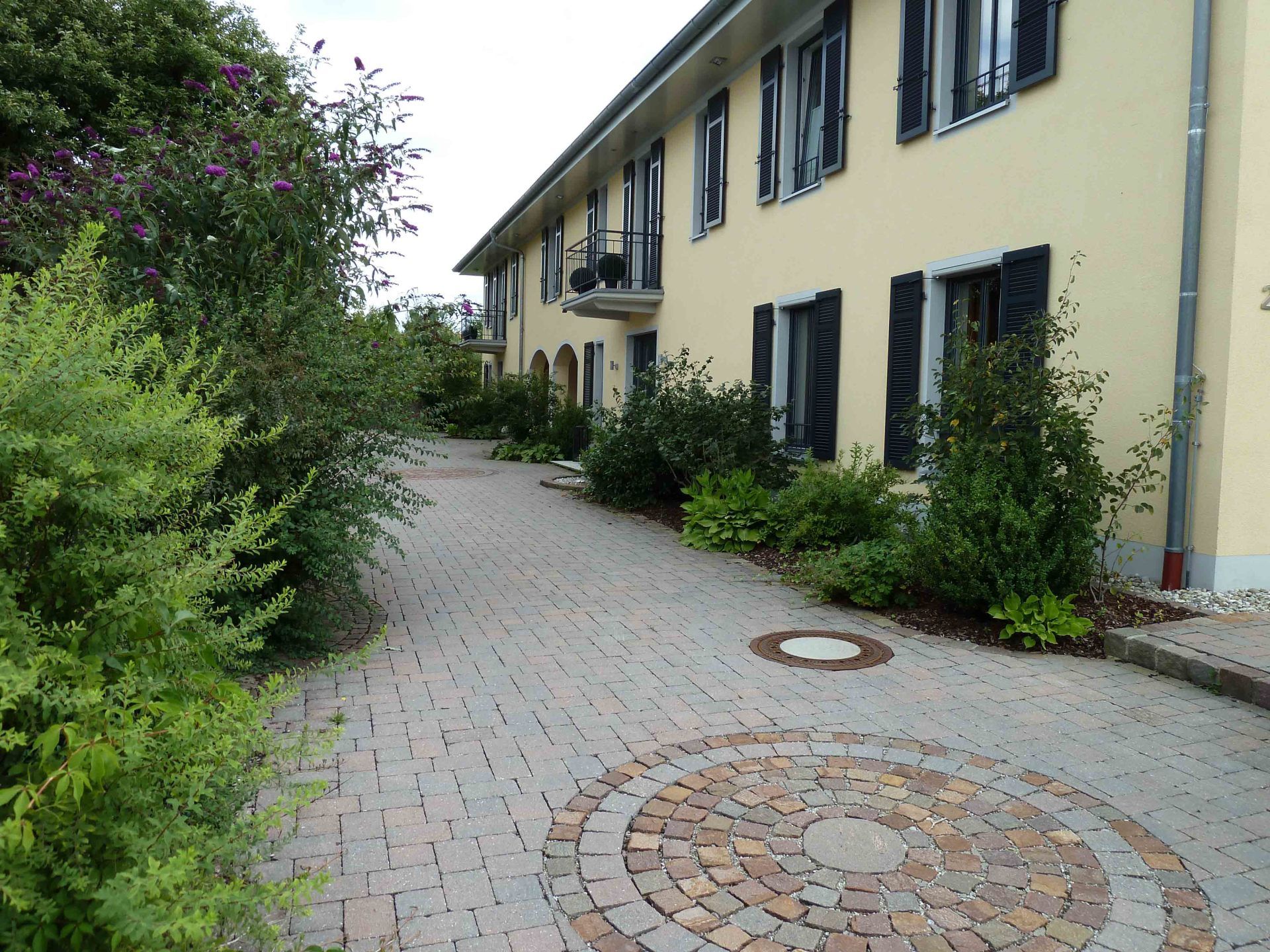 A brick walkway leading to a yellow building with black shutters