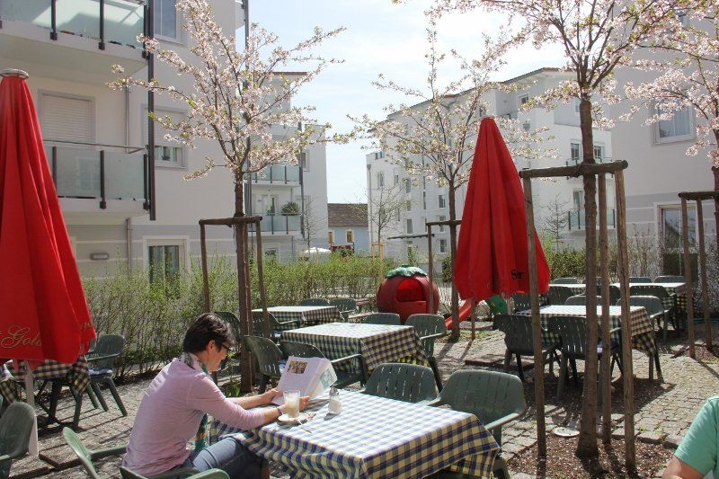 A woman is sitting at a table in a courtyard with red umbrellas.