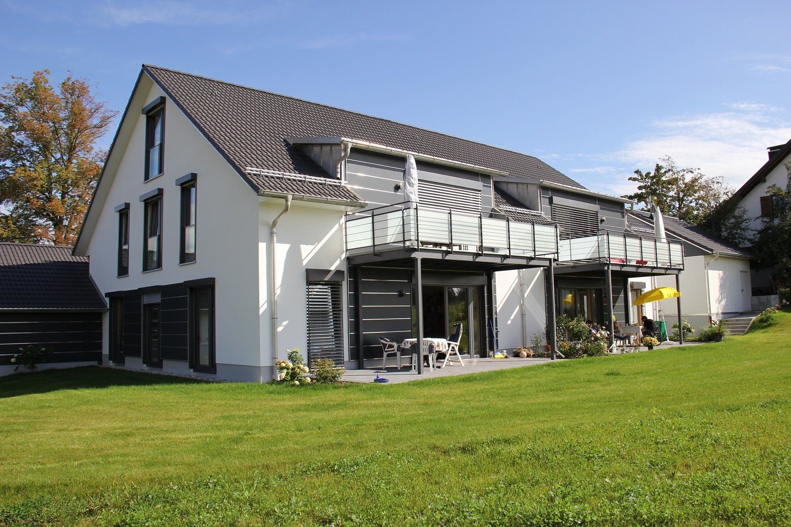 A large white house with a gray roof sits in the middle of a lush green field.