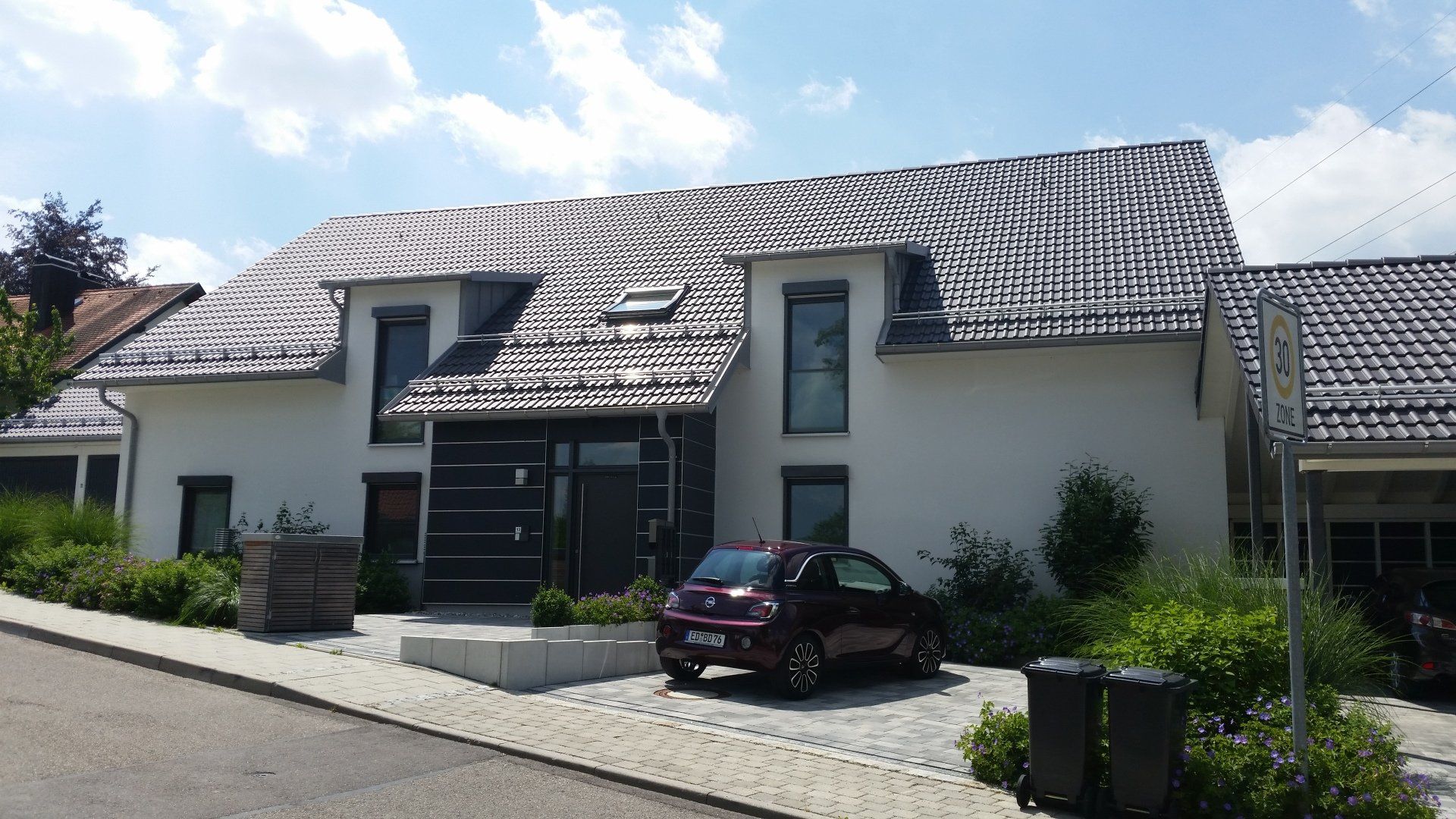 A red car is parked in front of a white house