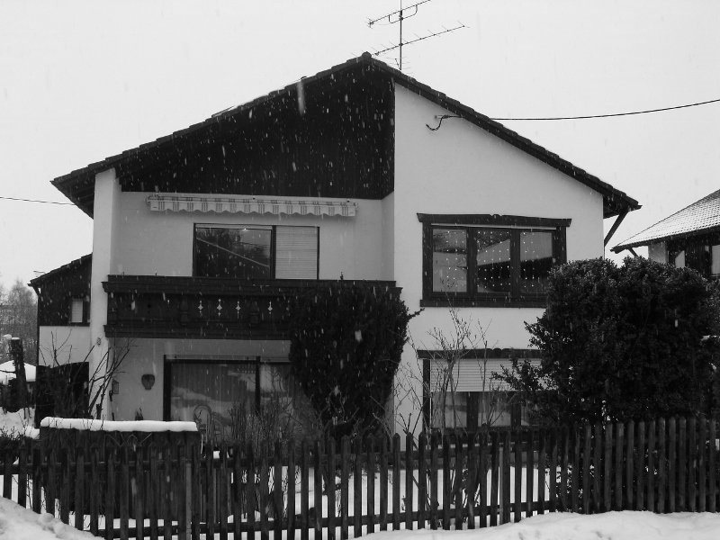 A black and white photo of a house with a fence in front of it