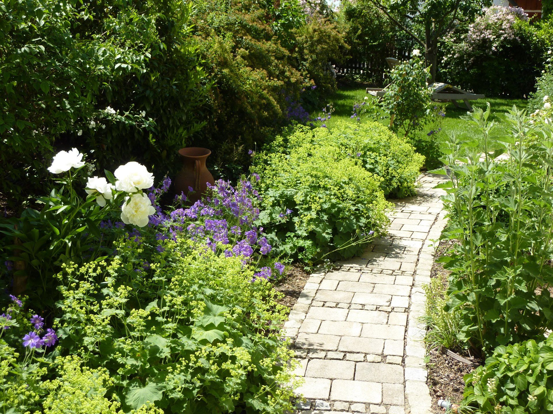 A brick path in a garden with purple and white flowers