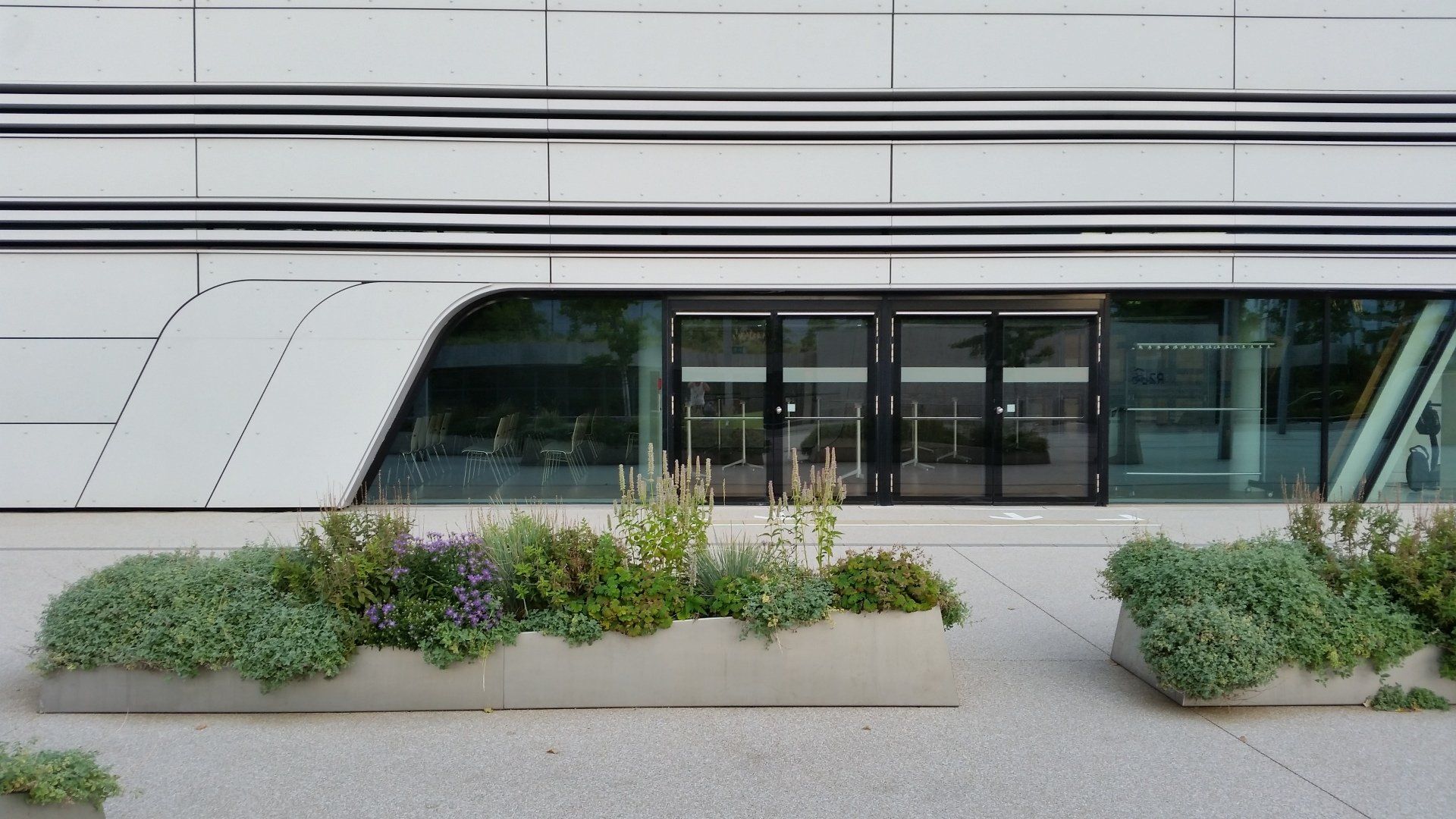 A building with a lot of windows and plants in front of it.