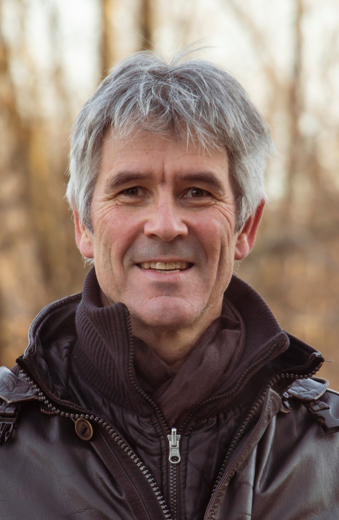 A man with gray hair and a black jacket is smiling for the camera.