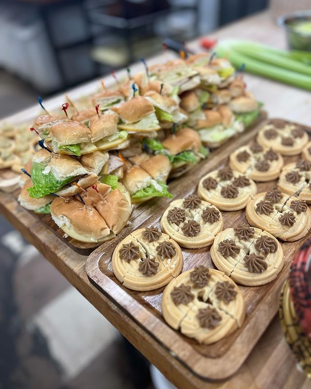A wooden tray filled with sandwiches and cookies on a table.