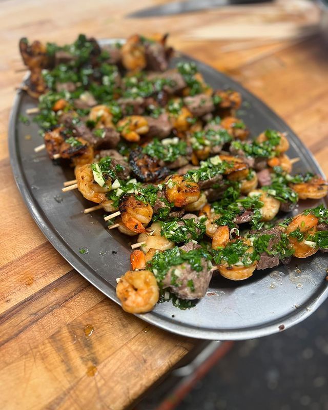 A tray of shrimp and meat skewers on a wooden table.