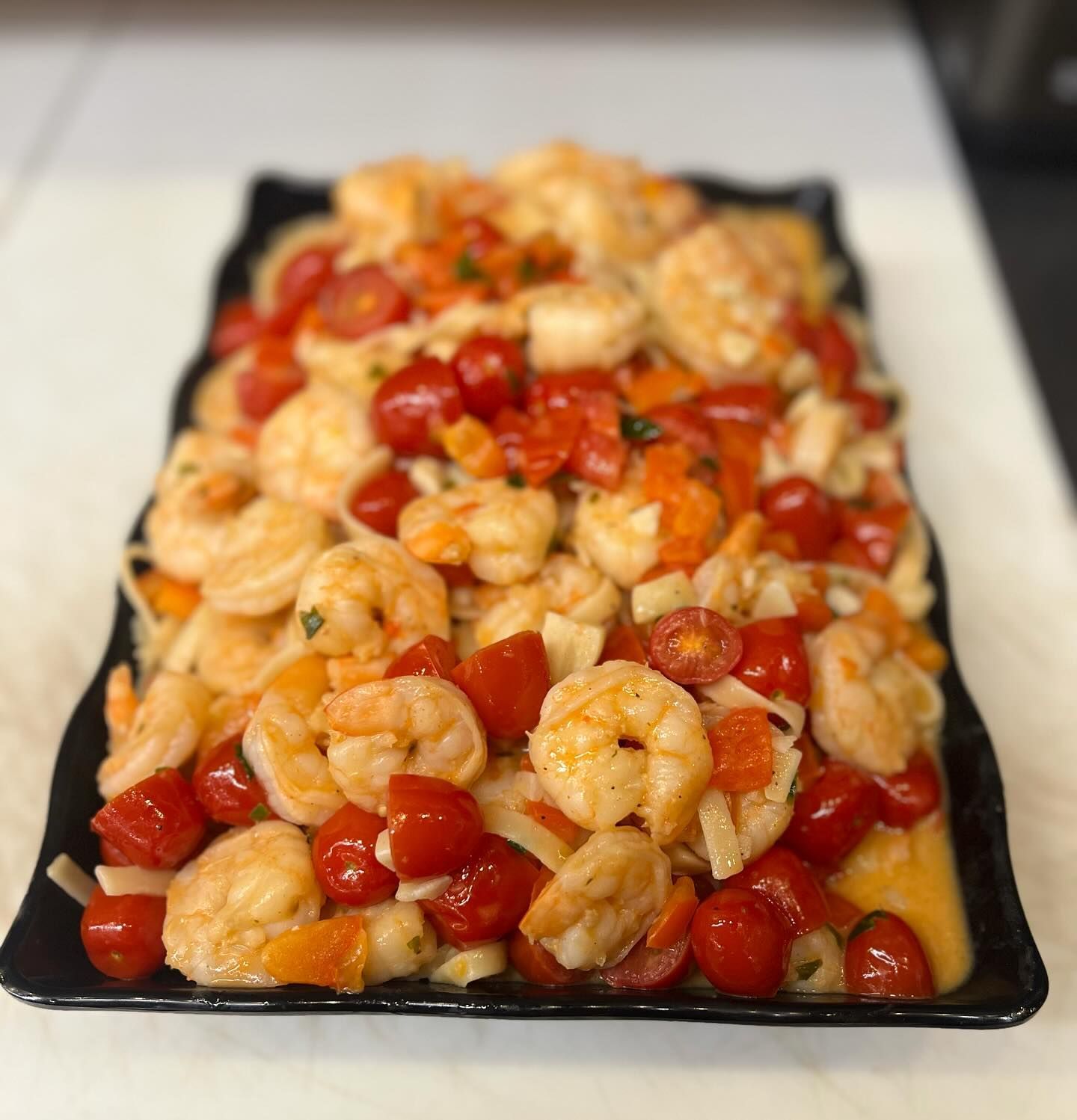 A black plate topped with shrimp and tomatoes on a table.